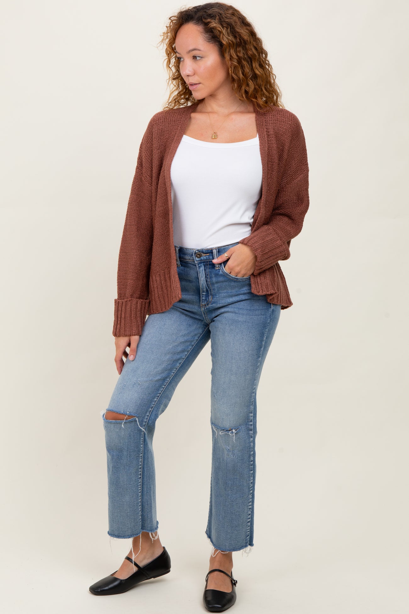 woman wearing a brown knit cardigan over a white tank top and blue high-waisted ripped jeans