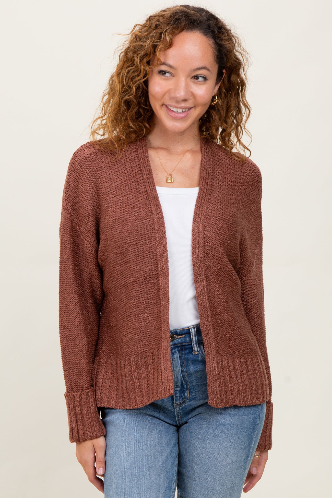 woman wearing a rust brown open front cardigan over a white top and blue jeans
