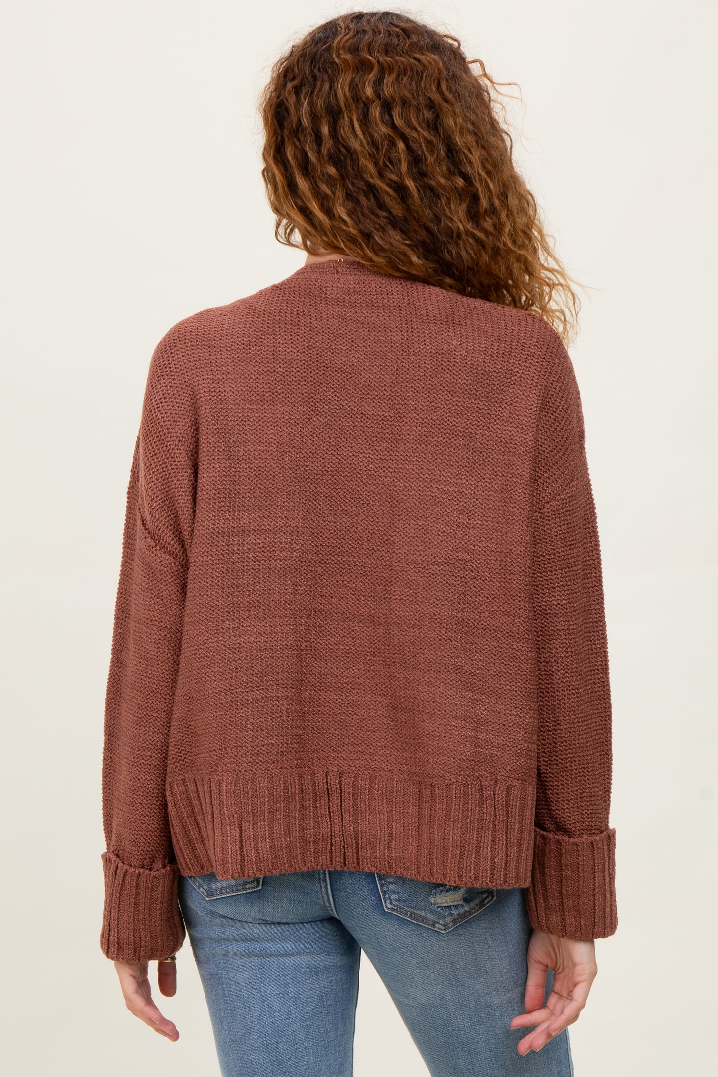 woman wearing a rust-colored oversized knit sweater with ribbed cuffs and a relaxed fit, shown from the back