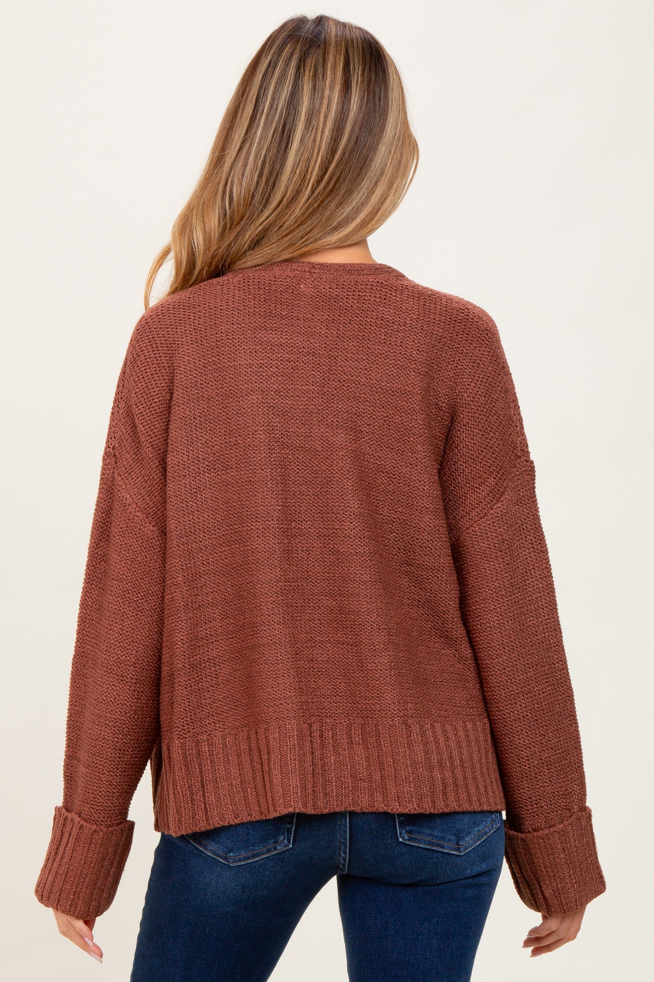woman wearing a rust colored oversized maternity sweater with ribbed details and a cropped back, shown from the back