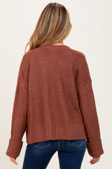 woman wearing a rust colored oversized maternity sweater with ribbed details and a cropped back, shown from the back