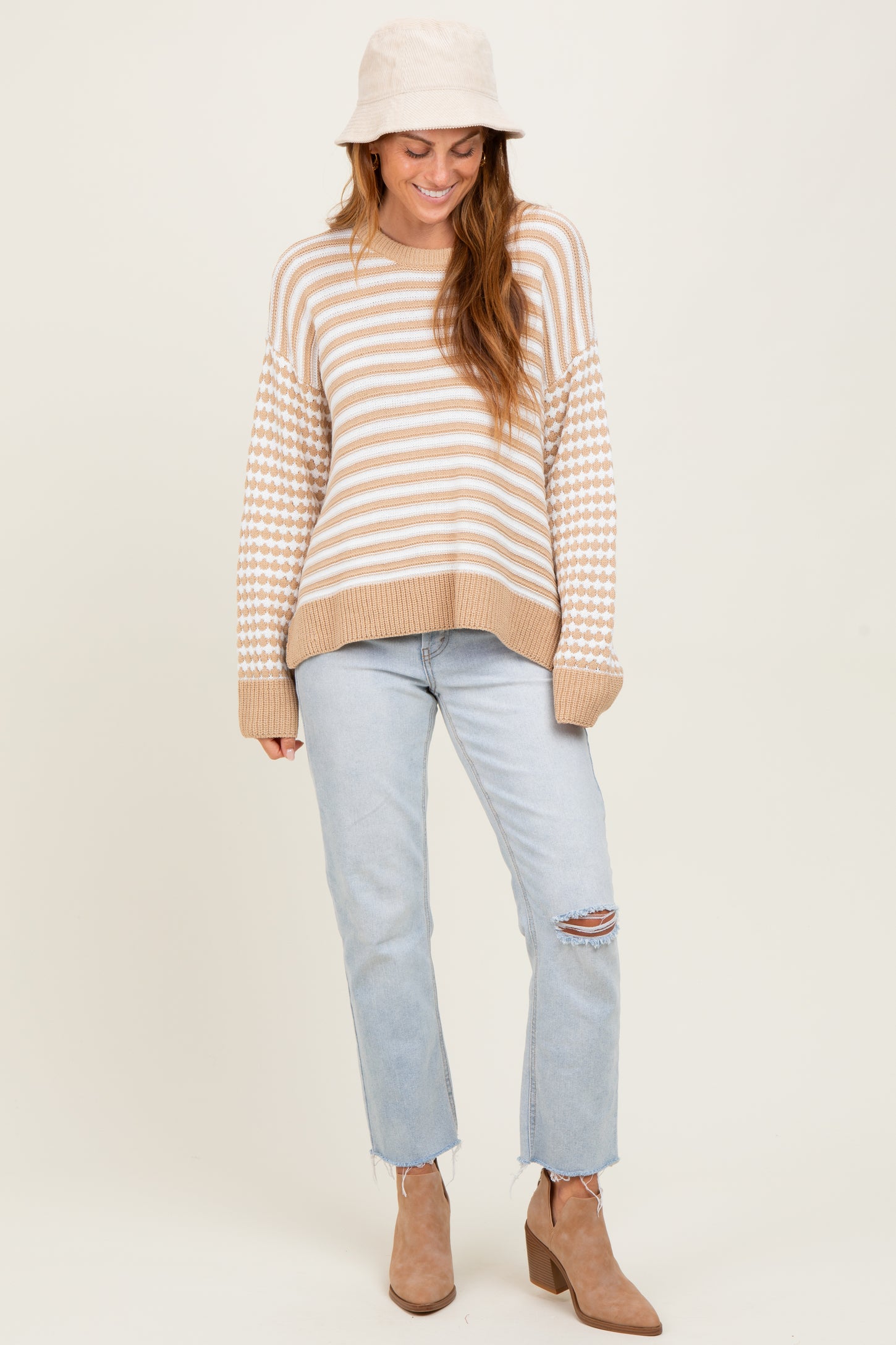 woman wearing a beige and white striped sweater with a checkered pattern and light blue distressed jeans