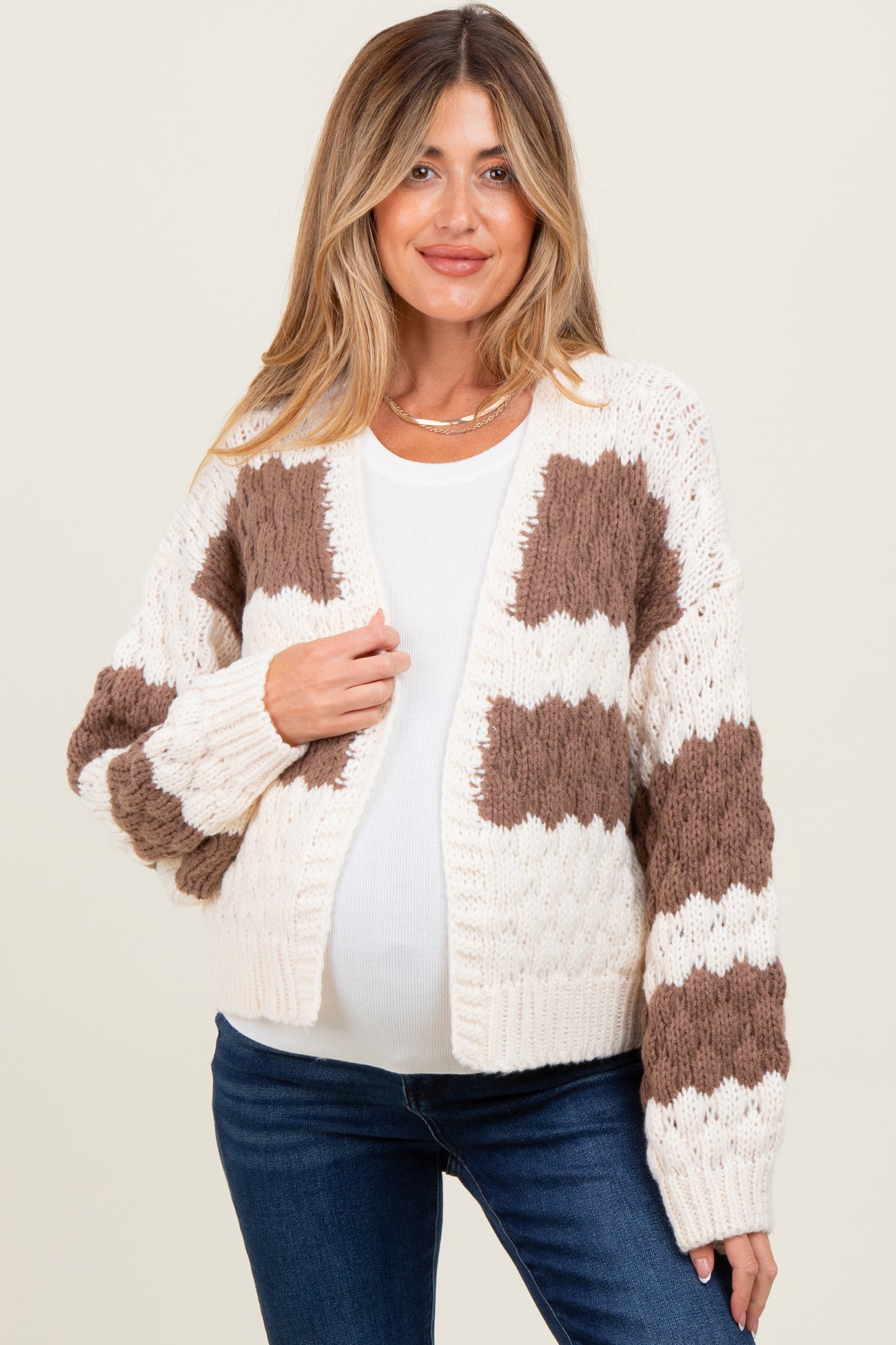 woman wearing a cream and brown patterned maternity cardigan over a white top, showcasing her baby bump