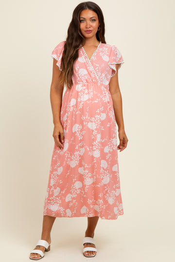 woman wearing a pink floral maternity dress with flutter sleeves and a wrap design, standing against a neutral background