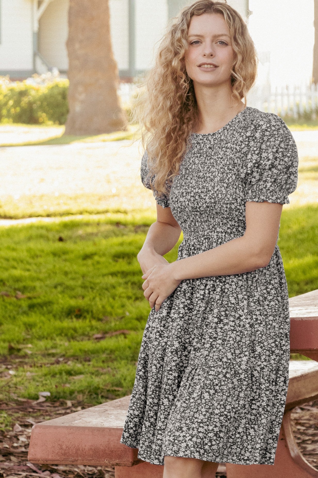 woman wearing a black and white floral puff sleeve dress, standing outdoors with a grassy background
