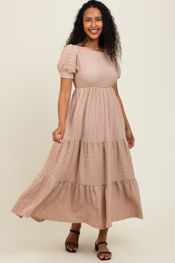 woman wearing a light pink tiered maxi dress with puff sleeves and a textured fabric, smiling and posing