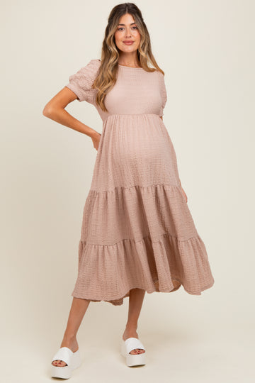 woman wearing a blush pink maternity dress with short puff sleeves and a tiered skirt, highlighting her baby bump