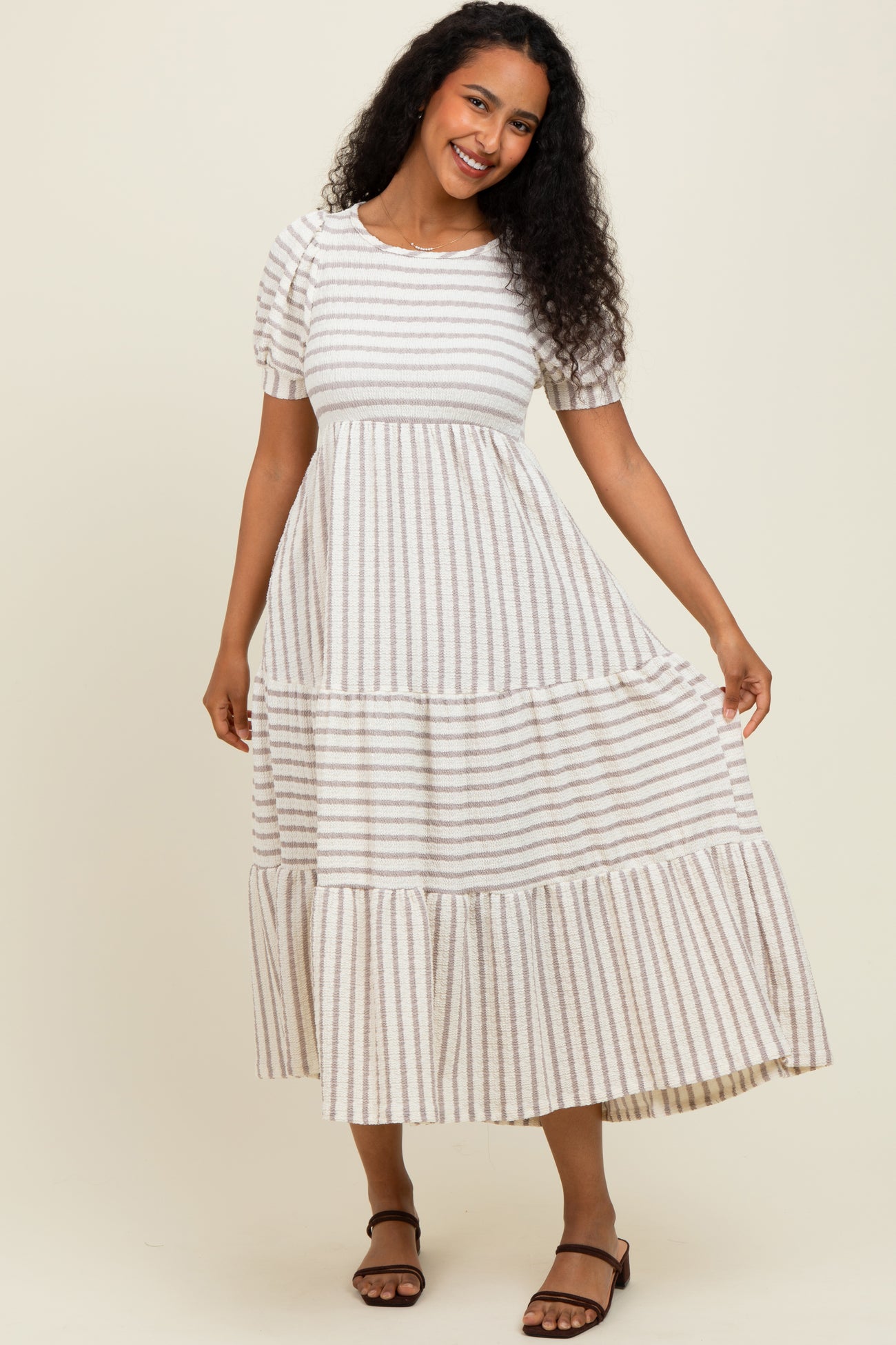 woman wearing a cream striped maxi dress with short sleeves and tiered detailing, smiling and posing