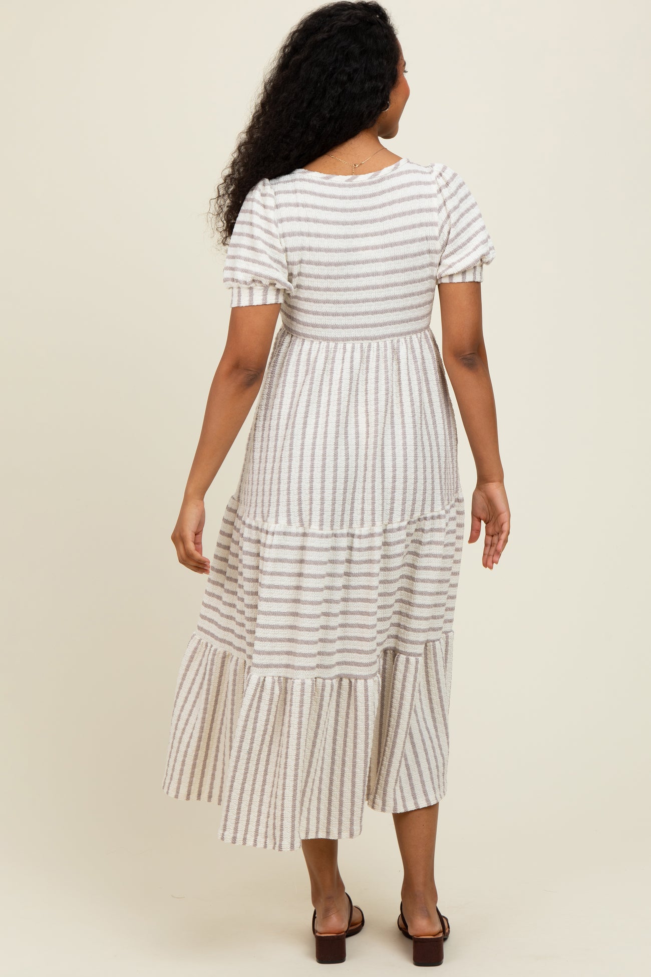 woman wearing a back view of a cream and gray striped tiered maxi dress with short sleeves and a relaxed fit