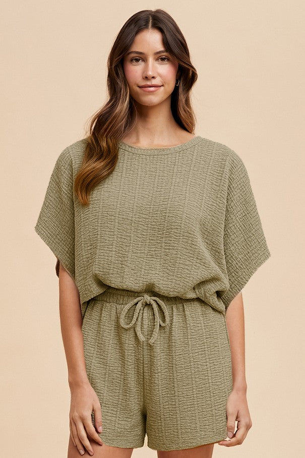 woman wearing an olive green textured short sleeve romper with a drawstring waist