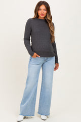 woman wearing a dark gray long sleeve maternity top with pockets and light blue wide leg jeans