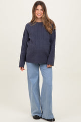 woman wearing a navy blue cable knit maternity sweater and light blue wide-leg jeans, with a visible baby bump