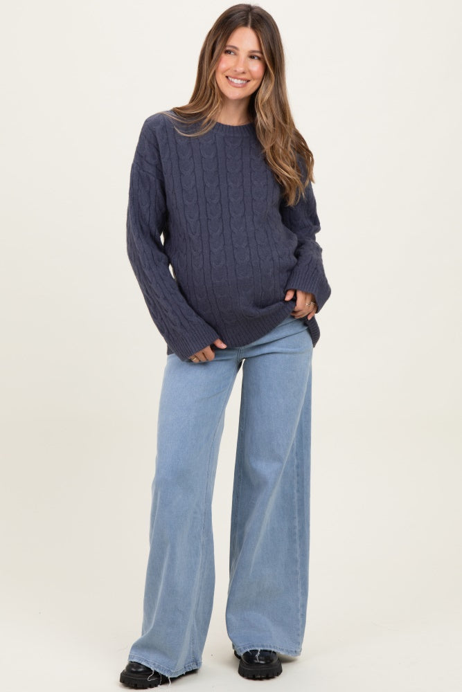 woman wearing a dark gray cable knit maternity sweater and light blue wide-leg jeans, showcasing her baby bump