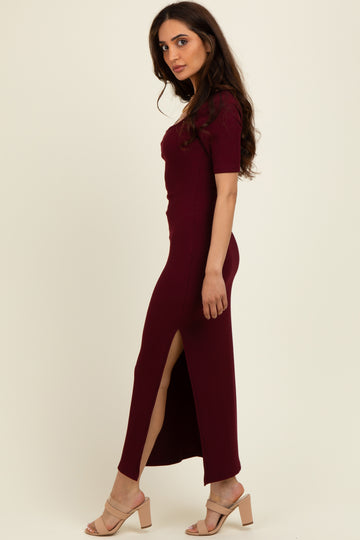 woman wearing a burgundy ribbed maxi dress with short sleeves and side slits, standing sideways in heels
