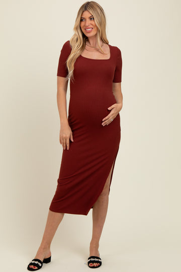 woman wearing a rust ribbed maternity dress with short sleeves and a side slit, holding her baby bump