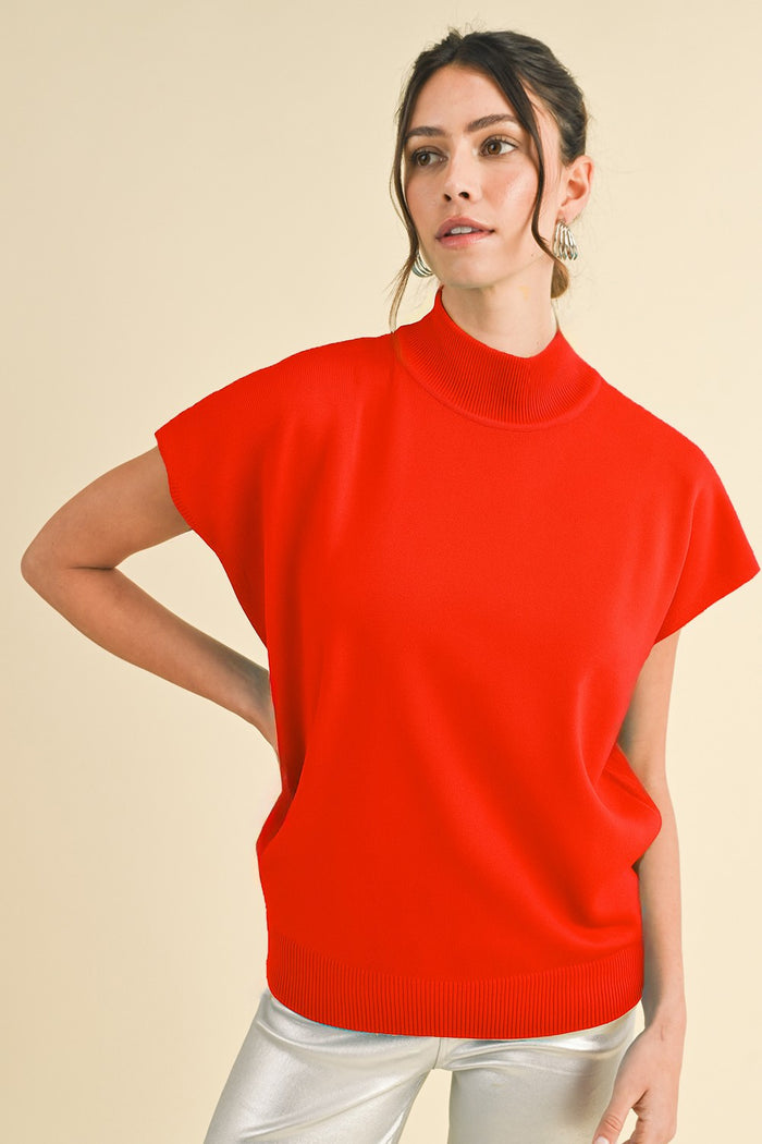 woman wearing a bright red short sleeve turtleneck sweater paired with shiny silver pants