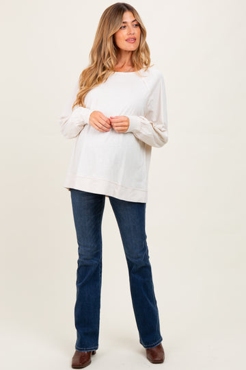 woman wearing a light beige maternity top and dark jeans, showing a baby bump