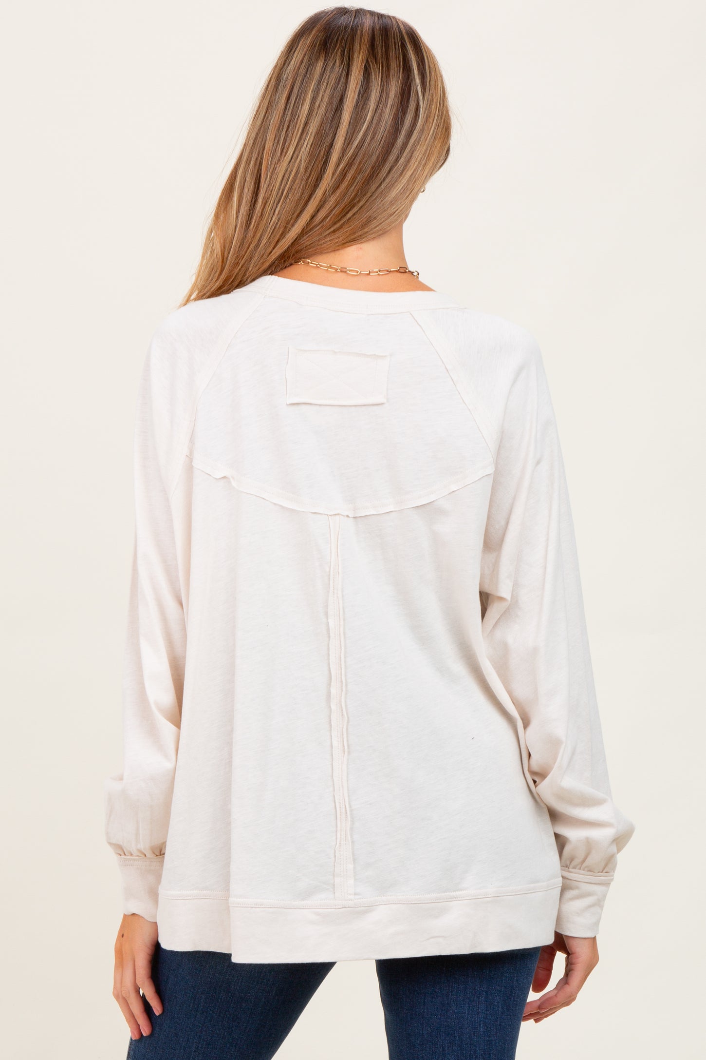 woman wearing a light beige long sleeve maternity top with a back pocket detail and relaxed fit
