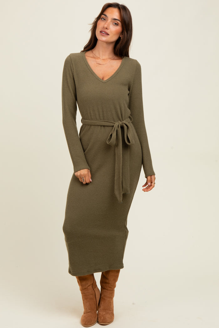 woman wearing an olive green ribbed midi dress with a v-neck and tie waist, standing and looking off to the side