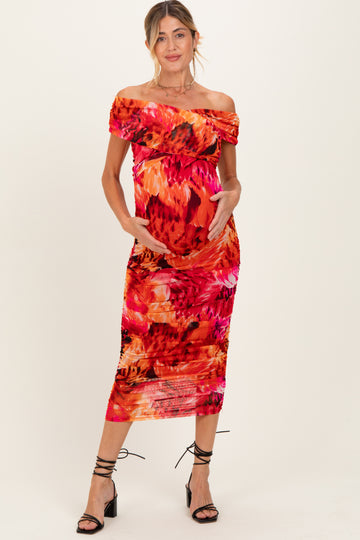 woman wearing a colorful off-the-shoulder maternity dress with floral print and holding her baby bump