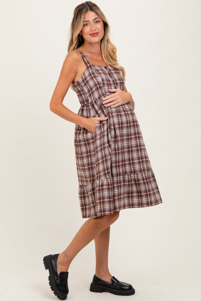 woman wearing a brown plaid maternity dress with pockets and a ruffled hem, showing her baby bump