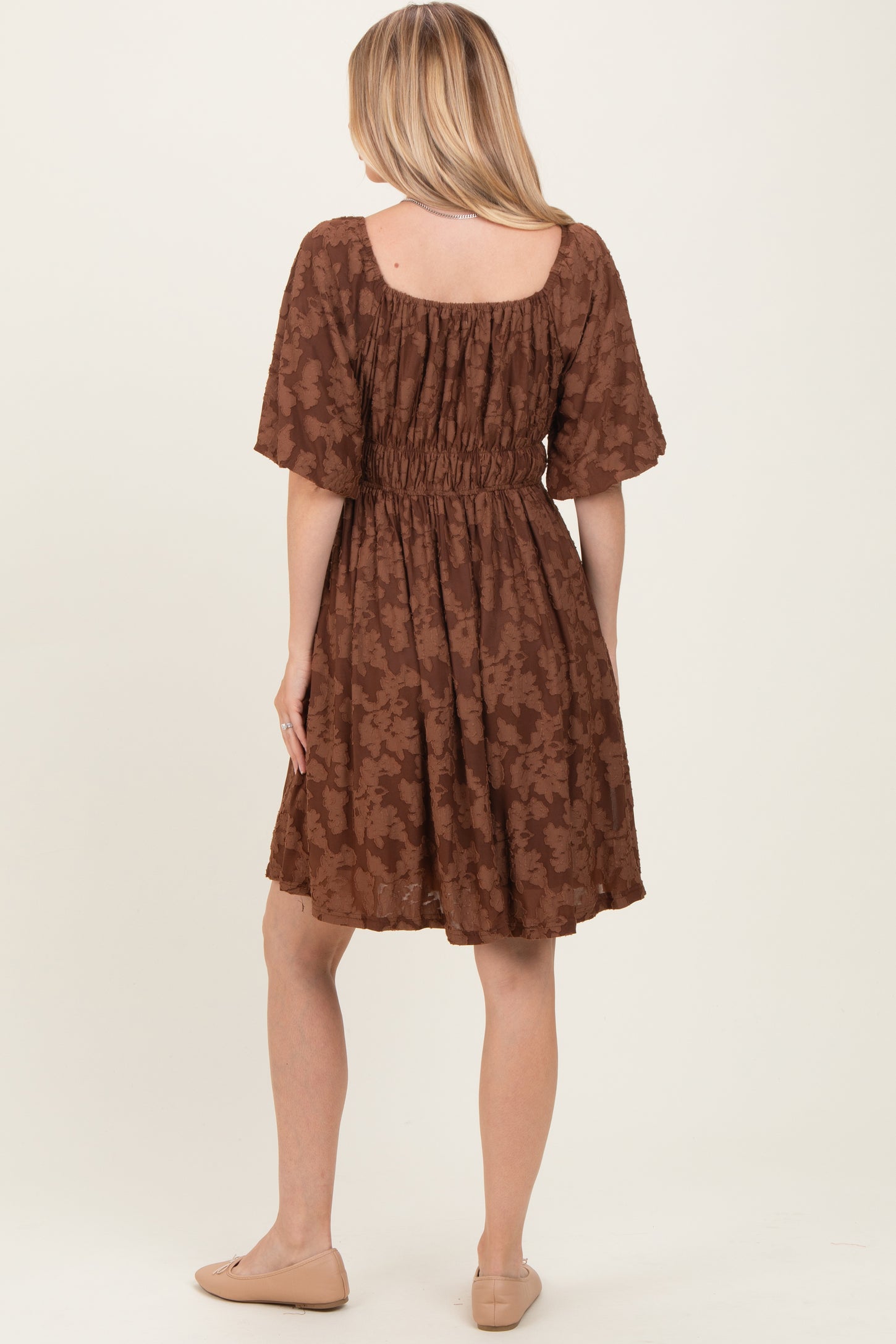 woman wearing a brown floral print short sleeve dress with a smocked waistband and a flared skirt, viewed from the back