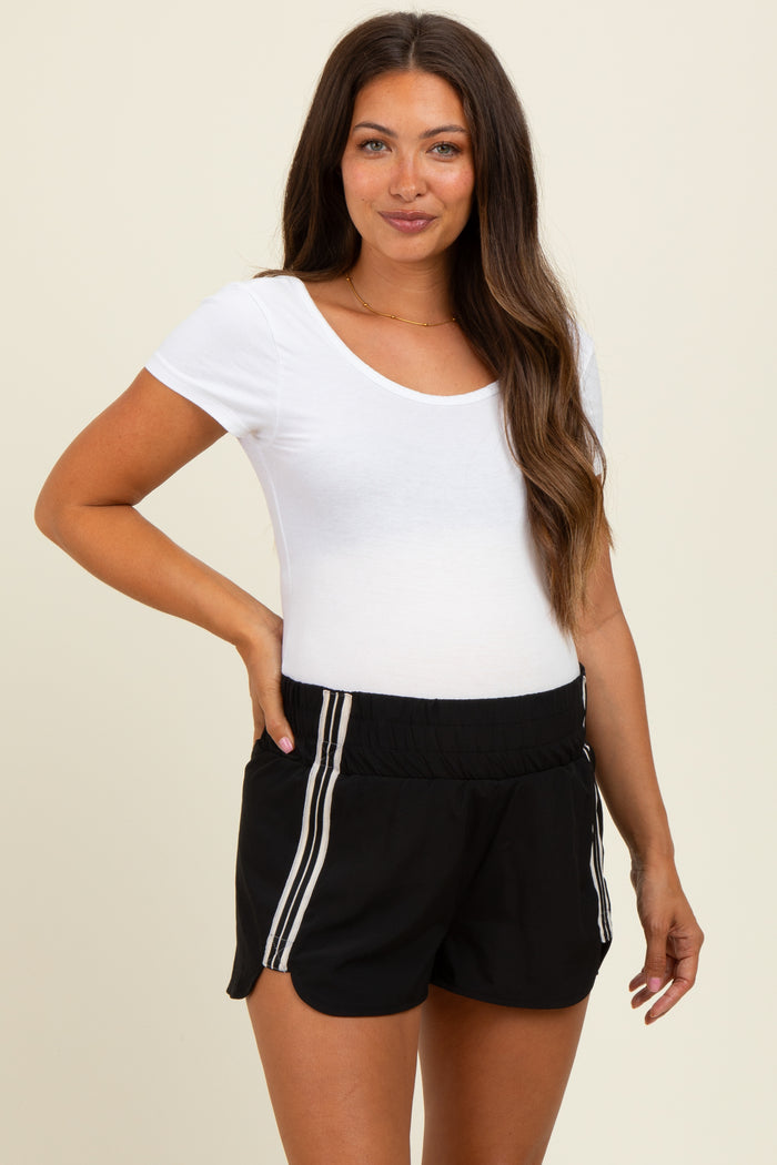 woman wearing a white short sleeve maternity top and black maternity shorts with side stripes, showing her baby bump
