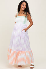 woman wearing a mint green and lavender striped maternity maxi dress with side pockets and a tiered orange striped hem