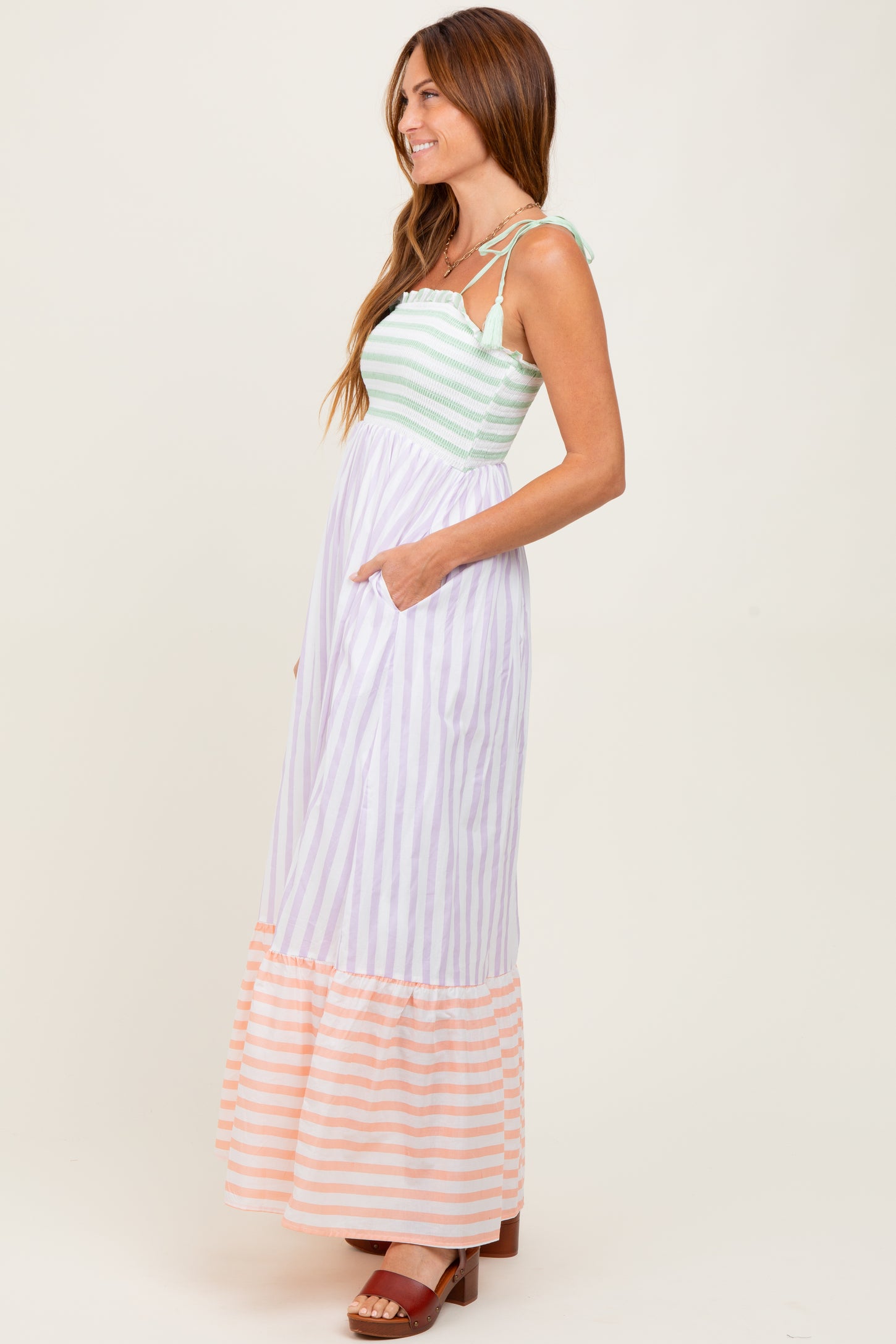 woman wearing a striped maxi dress with green, lavender, and peach colors, featuring pockets and adjustable straps