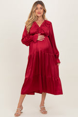 woman wearing a red satin maternity dress with long sleeves and tiered hem, showcasing her baby bump