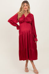 woman wearing a red satin maternity dress with long sleeves and a tiered skirt, showing her baby bump