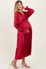 woman wearing a red long sleeve maternity dress with a tiered skirt and holding her baby bump
