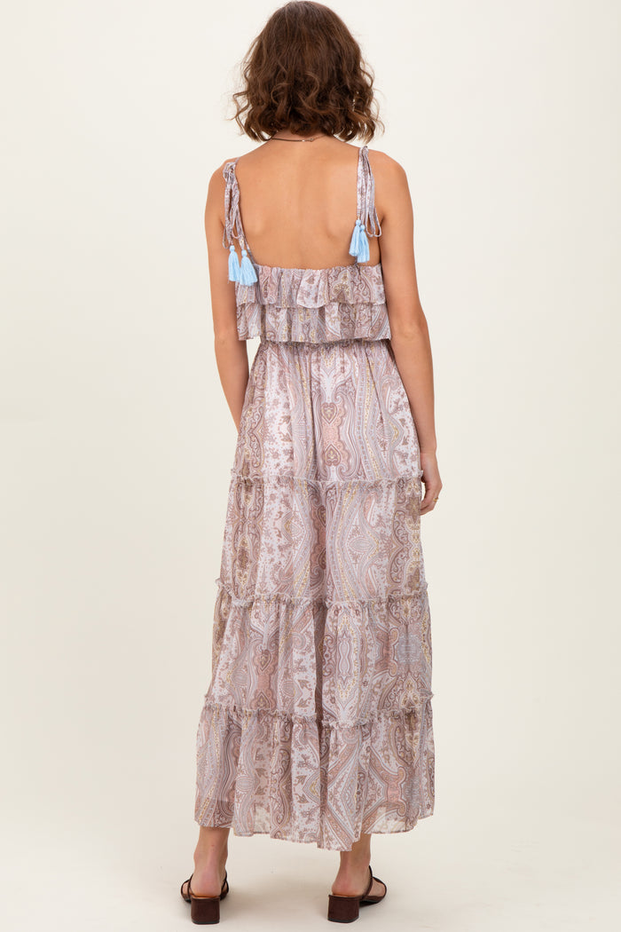woman wearing a backless tiered maxi dress with a paisley print and tassel detailing on the straps