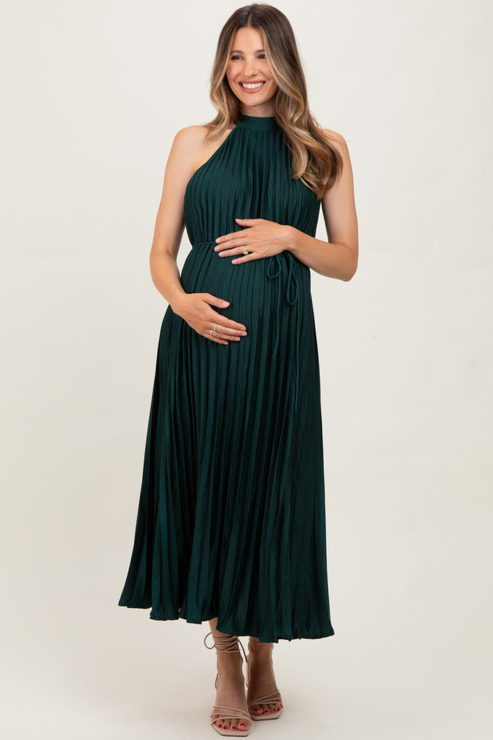 woman wearing a dark green pleated maternity dress and holding her baby bump