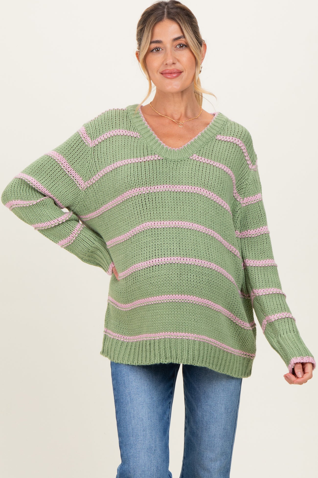 woman wearing a green and pink striped maternity sweater with a v-neck and relaxed fit, baby bump visible