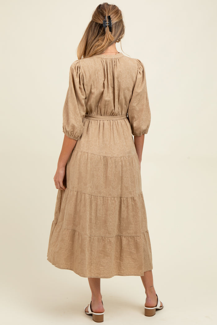 woman wearing a beige maternity tiered midi dress with puff sleeves and a tie waist, showing her baby bump from the back