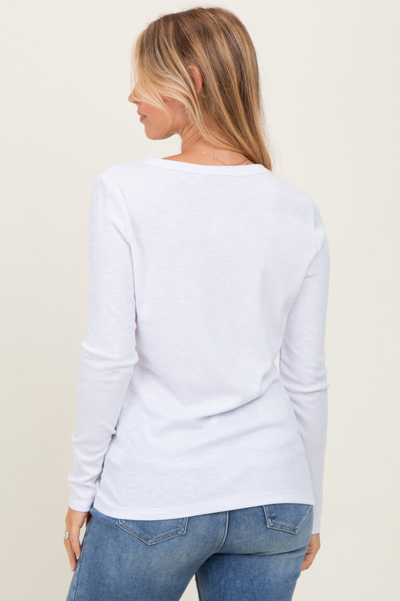 woman wearing a white long sleeve top, showing the back view, paired with light blue jeans
