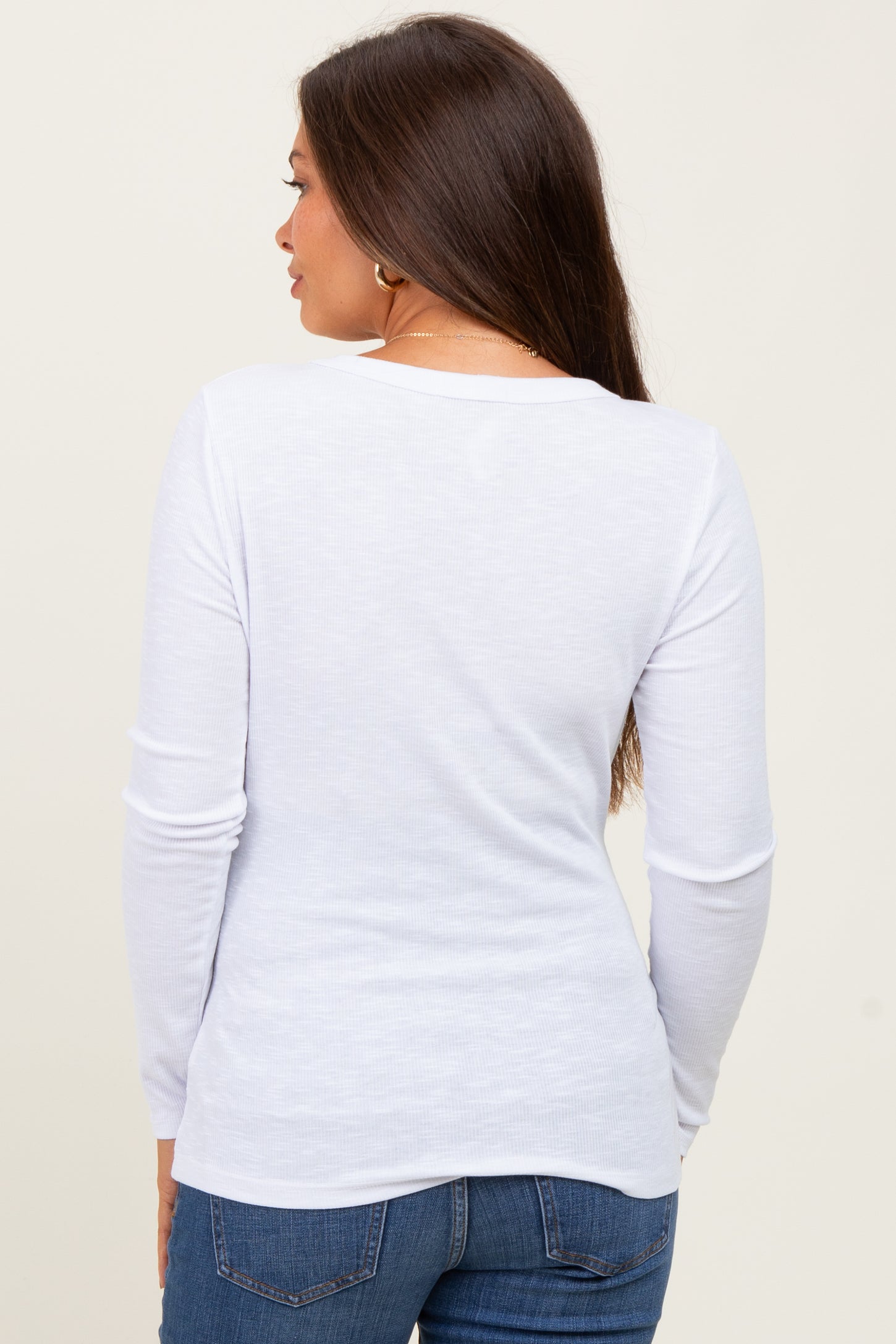 woman wearing a white long sleeve maternity top, seen from the back, paired with blue jeans