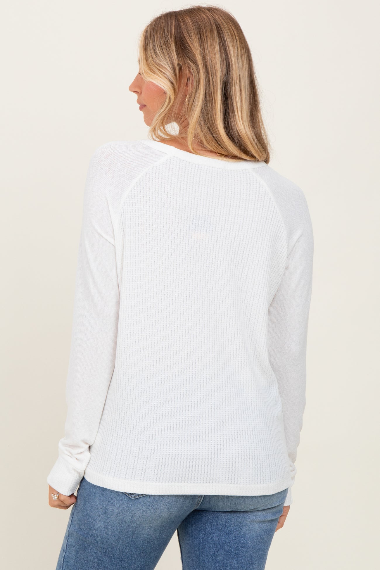 woman wearing a white long sleeve ribbed top, viewed from the back, paired with blue jeans