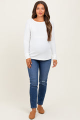 woman wearing a white long sleeve ribbed maternity top and blue distressed maternity jeans, showcasing her baby bump
