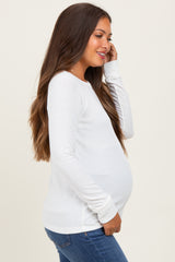 woman wearing a white long sleeve maternity top and gently holding her baby bump