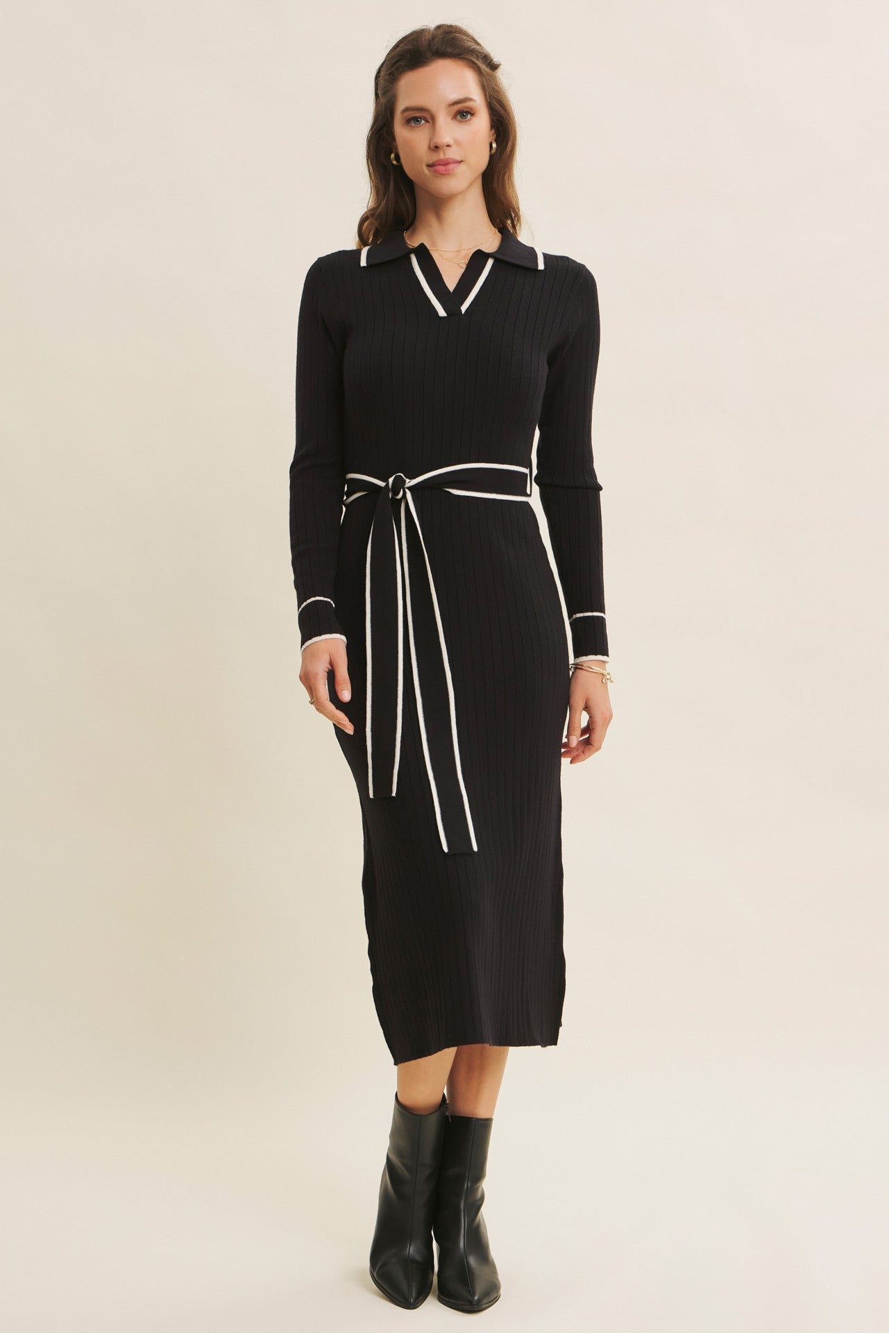 woman wearing a black ribbed long sleeve dress with a collar and contrasting white details, styled with a tie belt