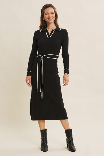 woman wearing a black ribbed midi dress with a collar, long sleeves, and a white tie belt, paired with black ankle boots