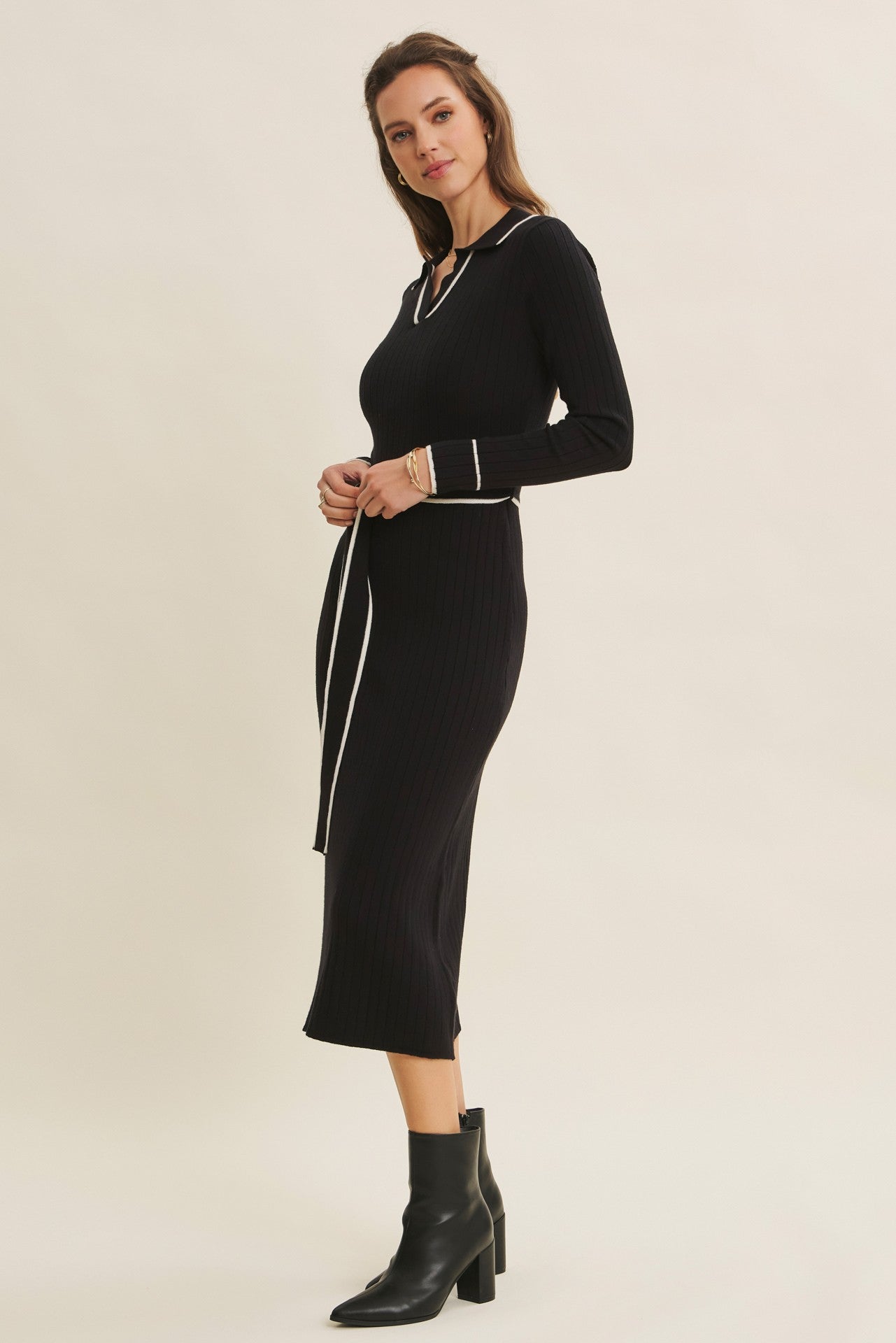 woman wearing a black ribbed knit midi dress with a v-neck and white trim, styled with ankle boots