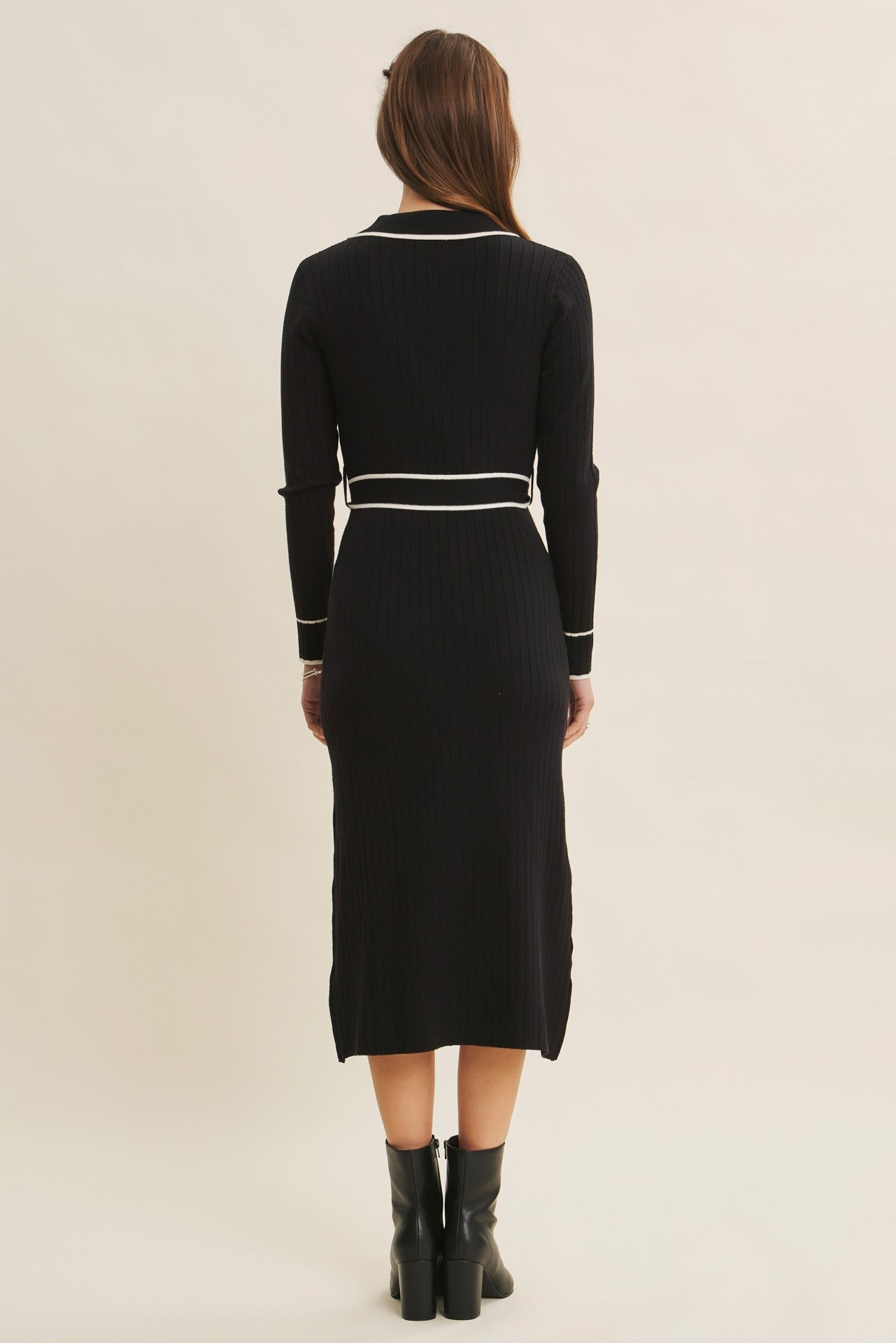 woman wearing a black ribbed midi dress with long sleeves and white accent details, shown from the back