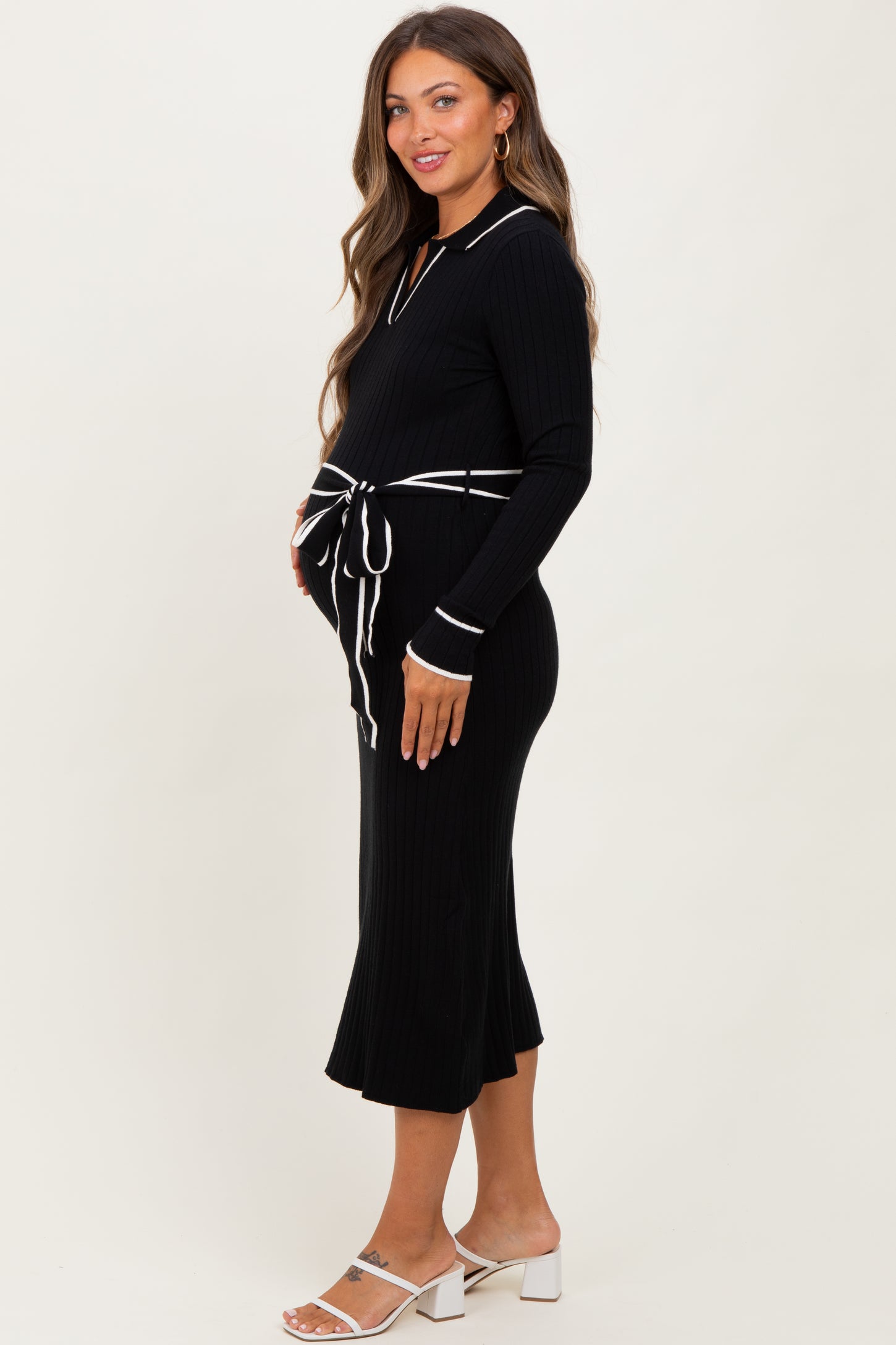 woman wearing a black ribbed maternity dress with white collar and tie waist, showcasing her baby bump