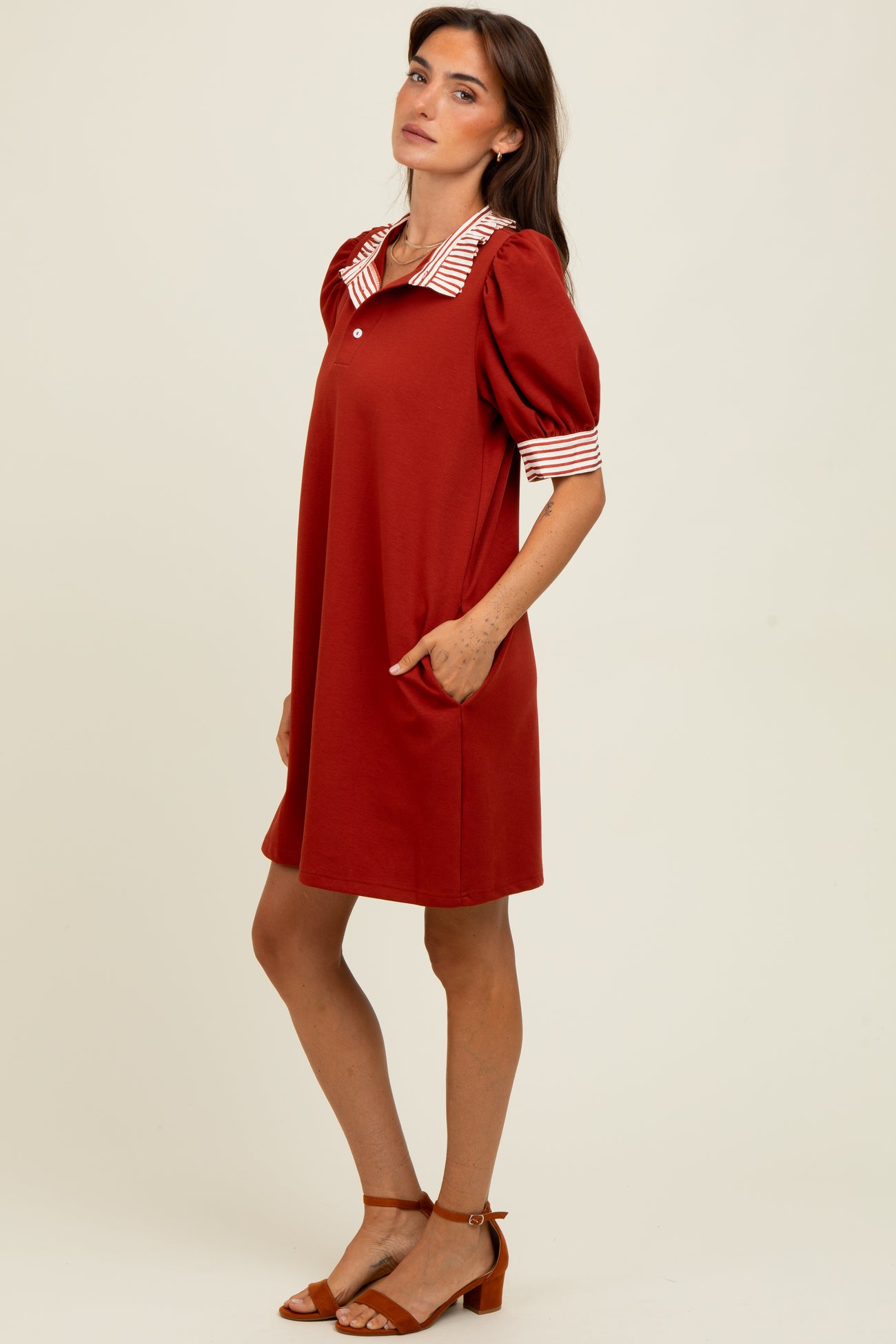 woman wearing a rust colored short sleeve dress with a striped collar and pockets, styled in a relaxed fit