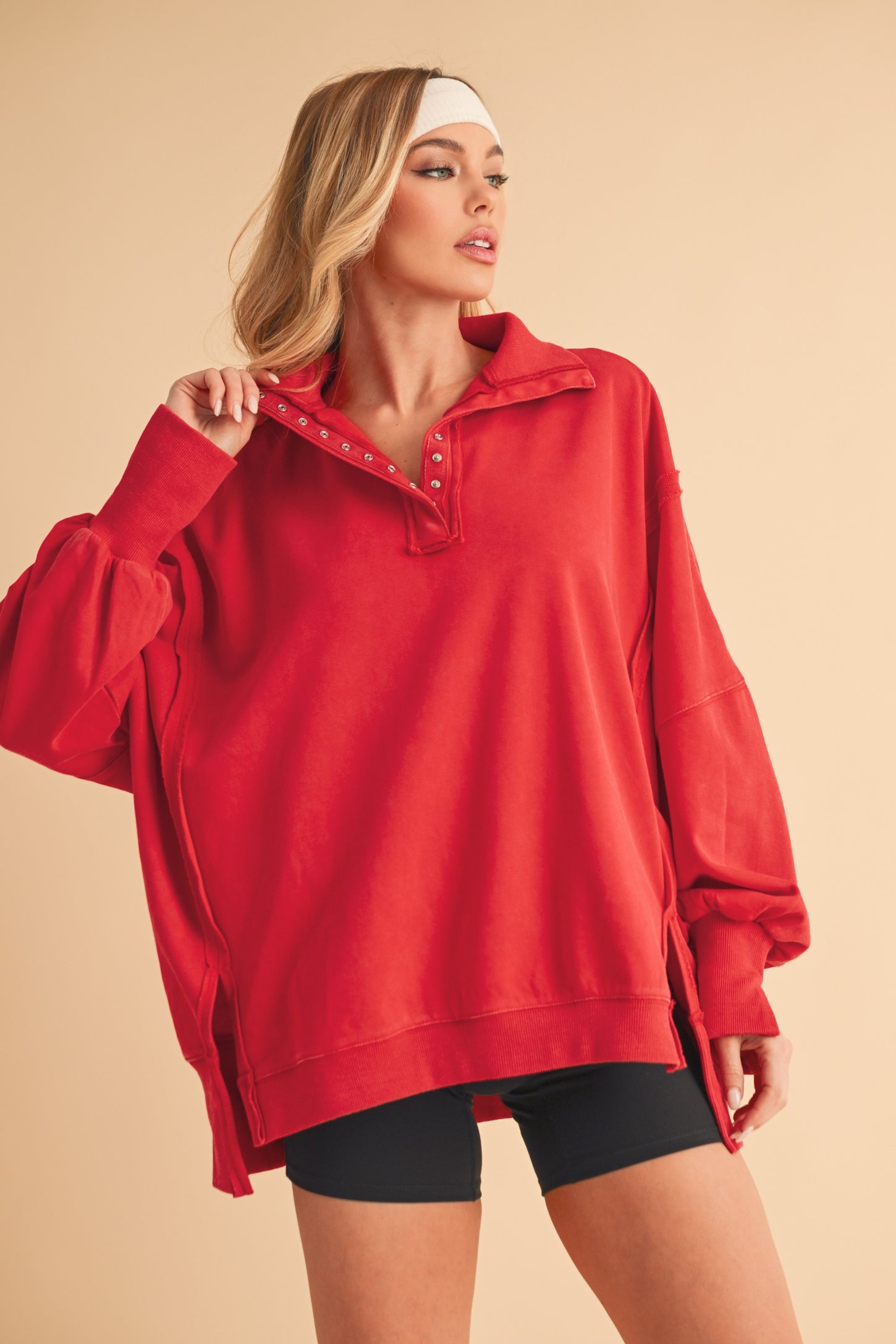 woman wearing a red oversized pullover sweatshirt with a collar and button details, paired with black shorts