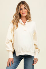 woman wearing a cream maternity pullover sweatshirt with a half-button placket and balloon sleeves, showing her baby bump