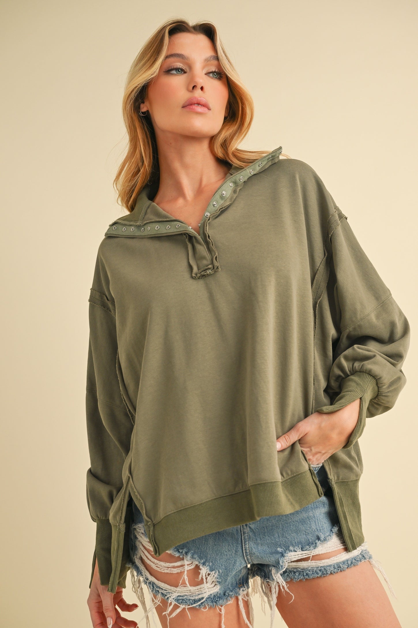 woman wearing an olive green oversized hoodie with a buttoned collar and distressed denim shorts